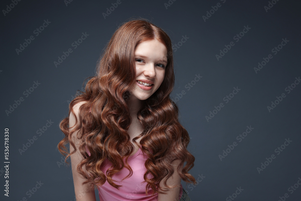 Fototapeta premium Portrait of smiling teenage girl with healthy wavy hair on dark grey background