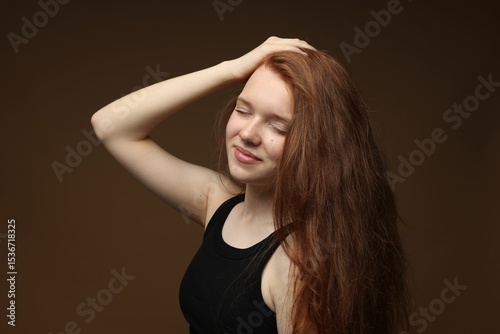 Beautiful teenage girl with healthy wavy hair on brown background
