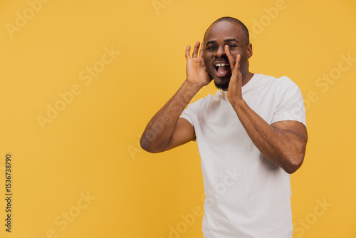 Young african american man shouting and cupping hands around mouth on yellow background