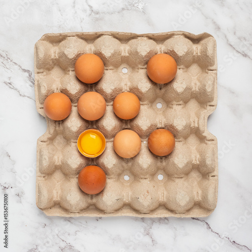 Egg box with an open egg on a white marble counter.