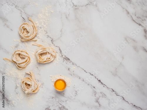 Rolled pasta over a marble surface with a raw egg. Flat lay with a bright background