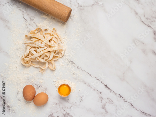 Fresh pasta over a kitchen counter with a rolling pin and some eggs