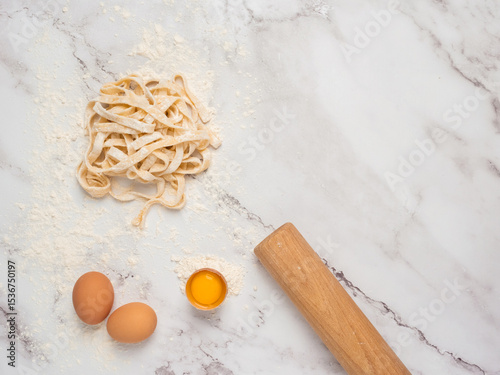 Fresh pasta over a kitchen counter with a rolling pin and some eggs