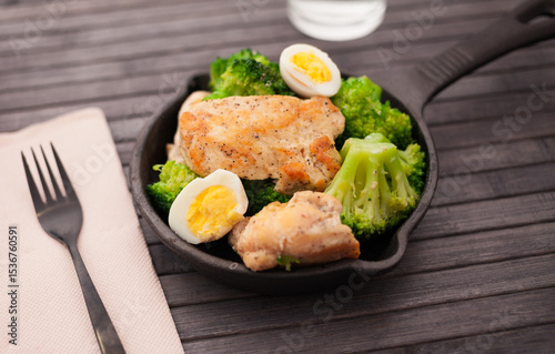 Chicken breast with broccoli and quail eggs in small cast iron skillet