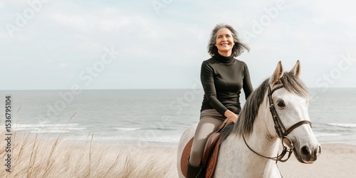 Mature caucasian female riding horse on beach, smiling in black sweater photo
