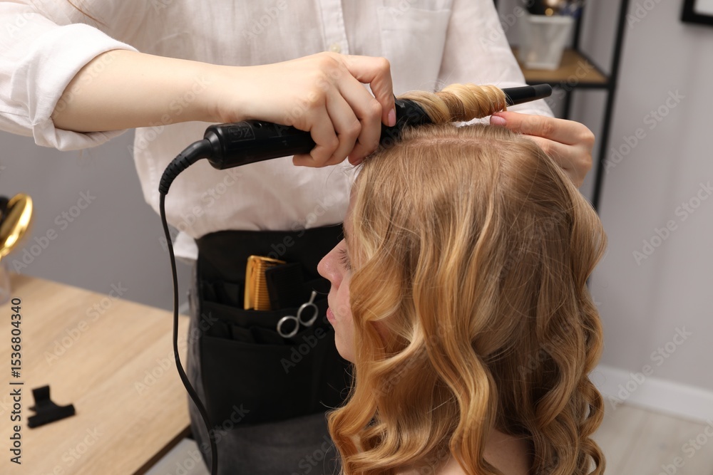 Fototapeta premium Hairdresser curling woman's hair in salon, closeup