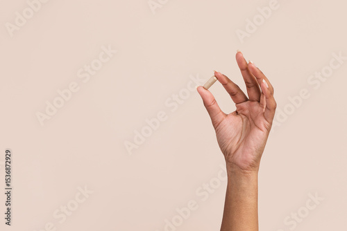 Black woman holding supplement pill in hand on tan background with copy space