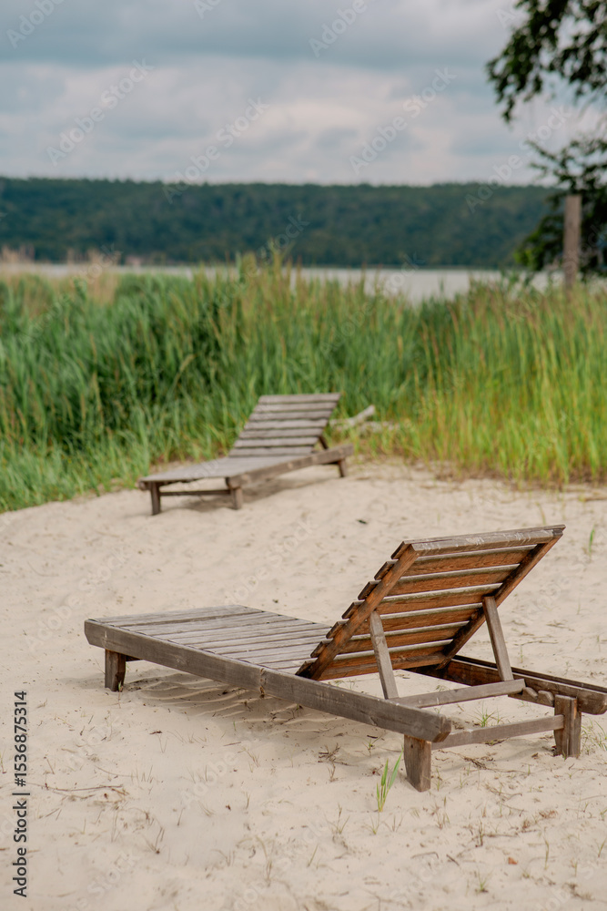 Obraz premium Wooden lounger on a sandy beach by the lake