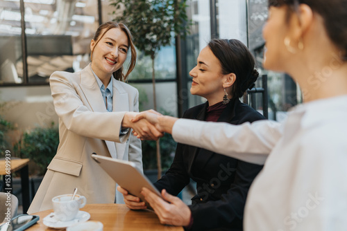Foto Two businesswomen shaking hands in a cafe while discussing during a meeting