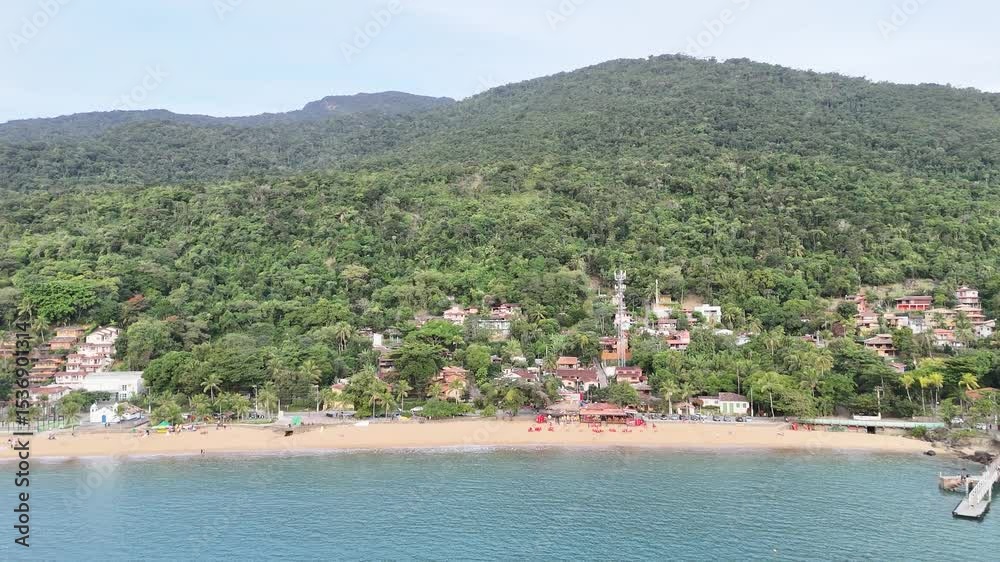 Visão aérea da Praia Grande em Ilhabela, SP, com faixa extensa de areia, mar aberto, vegetação tropical e turistas aproveitando o sol no litoral paulista