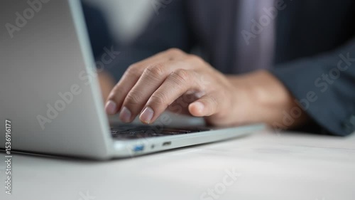 Professional businessman working intensely on laptop, hands typing rapidly while browsing internet and searching critical business information in modern corporate workplace
