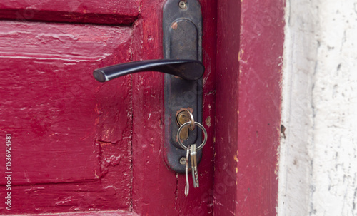 Keys inserted into a black lock in an old red wooden door