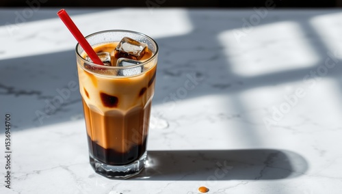 Iced coffee with milk and ice cubes in a tall glass on marble  
