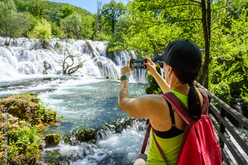 Family visiting famous Martin Brod waterfall in national park Una River in Bosnia and Herzegovina. Tourists taking photos of the amazing waterfall Martin Brod and river Una in Bosnia.