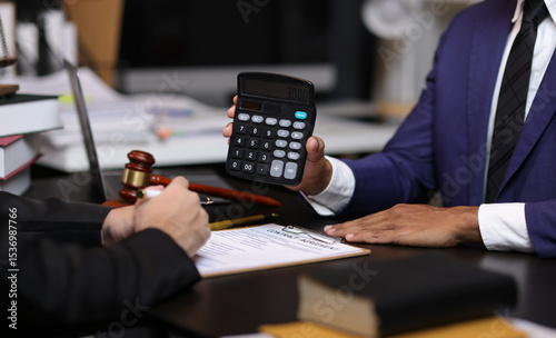 Lawyers discussing legal fees using calculator in law office. Two lawyers are discussing legal fees for a new contract using a calculator, highlighting the financial aspects of legal representation.
