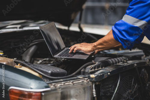Car mechanic running diagnostics on vehicle using laptop.