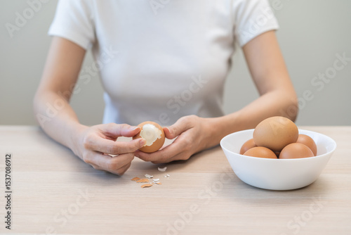 Protein in food, keto diet asian young woman hand peeling, shelling chicken boiled egg, prepares ingredient for breakfast meal on table at home. Removing egg shell, cleaning egg, health care concept.