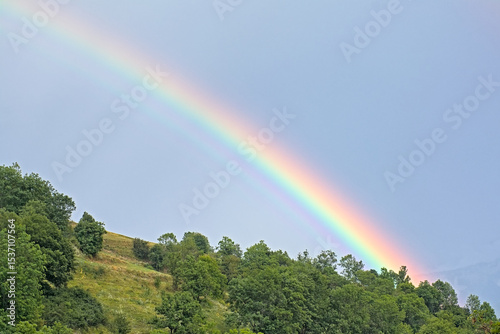 Rainbow against a dark stormy sky over a green mountain slope with trees in the Alps, La Vanoise nature reserve, France 