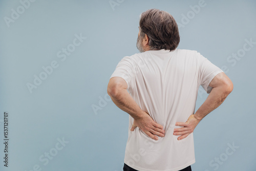 Senior man suffering from back pain on light blue background