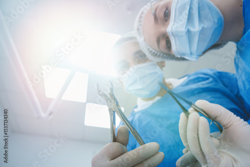 dentist surgeon holding teeth for tooth extraction with assistant leaning and looking at patient.  Medical team performing surgery