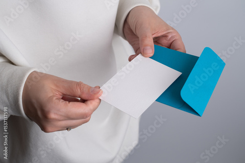 Girl holding a holiday card in her hands while sitting on the sofa. Cute message for invitation on paper. Empty space for text.
