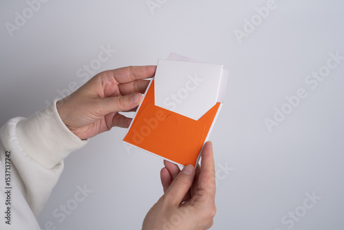 Girl holding a holiday card in her hands while sitting on the sofa. Cute message for invitation on paper. Empty space for text.