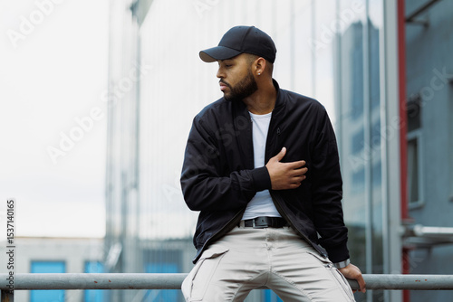 Photos Stylish african american man in baseball cap sitting on railing on urban street