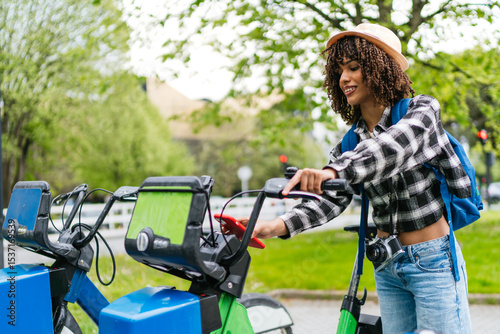 Young latin tourist unlocking a bike sharing in the city using her smartphone app, sustainable mobility concept photo
