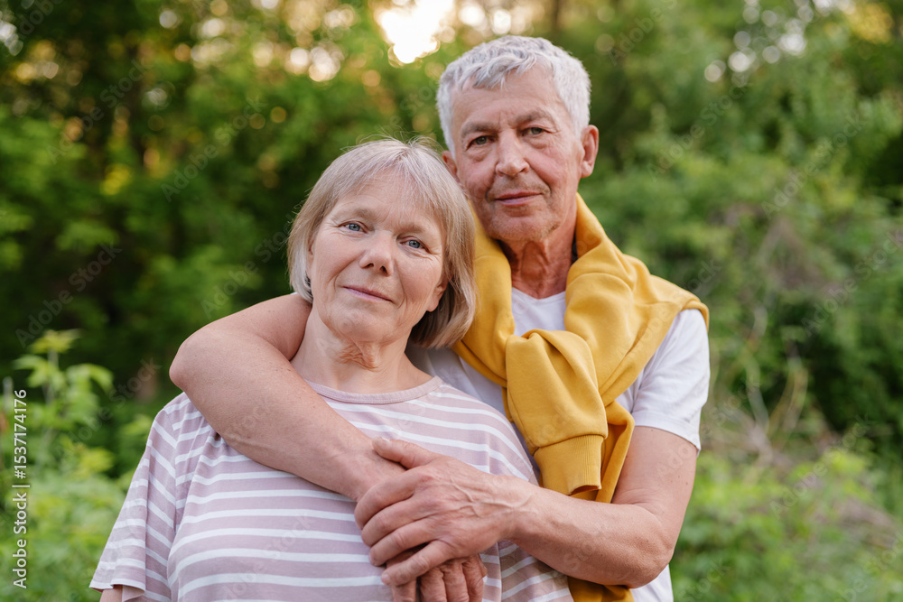 Senior couple embracing and looking at the camera with gentle smiles, surrounded by green nature. Senior couple embracing and looking at the camera with gentle smiles, surrounded by green nature.