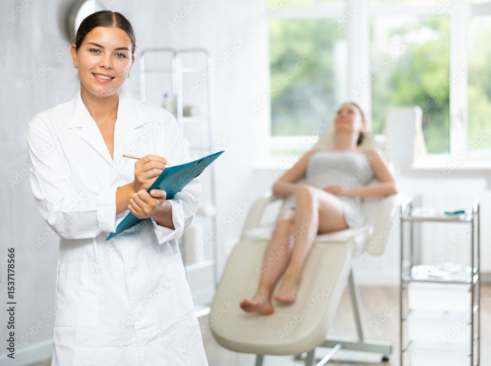 Obraz premium Young woman cosmetologist in uniform makes notes in medical room