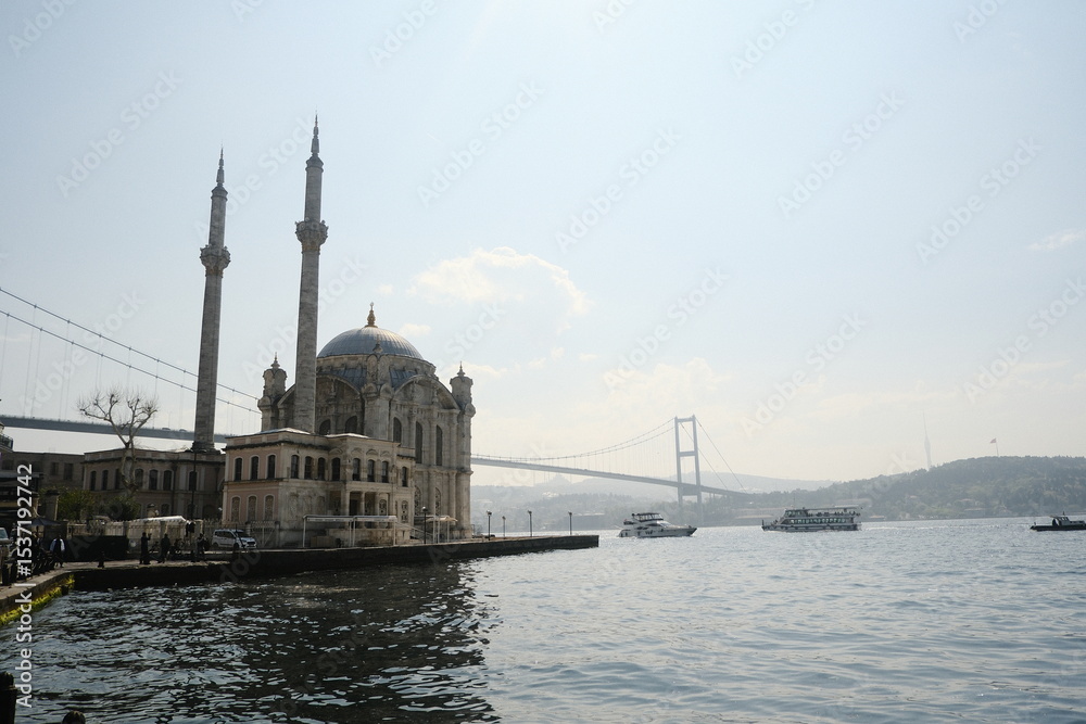 Naklejka premium Historic mosque overlooks the Bosphorus with a bridge in the background on a sunny day in Istanbul