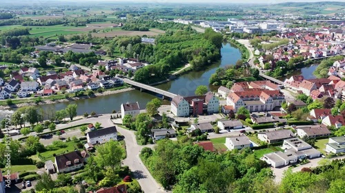 Luftaufnahme von Donauwörth mit roten Dächern, historischen Gebäuden und einem markanten Turm, eingebettet in eine grüne Landschaft. Die Stadt bietet eine charmante Kulisse. 