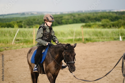 Prague, Czech Republic - May 31, 2025: Young boy riding a black horse in a riding arena, wearing safety gear and enjoying the experience of learning horse riding outdoors photo