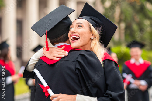 Cheerful young blonde lady hugging her black boyfriend while graduation ceremony at university campus. Two happy multiracial students greeting each other with successful graduation, closeup