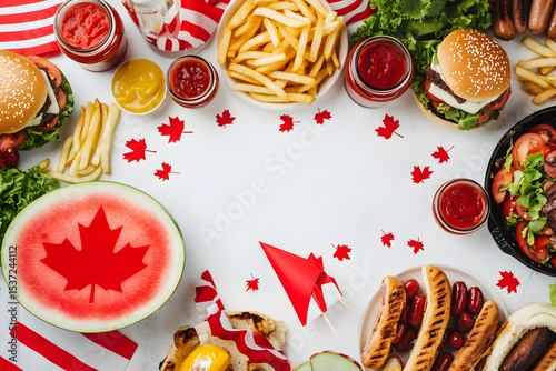 Set of various Canada Day bbq food. Picnic party table with maple leaf shaped watermelon, flags, burgers, hot dogs, fries and sauces, cold drinks, white table with red decor, top view copy space photo