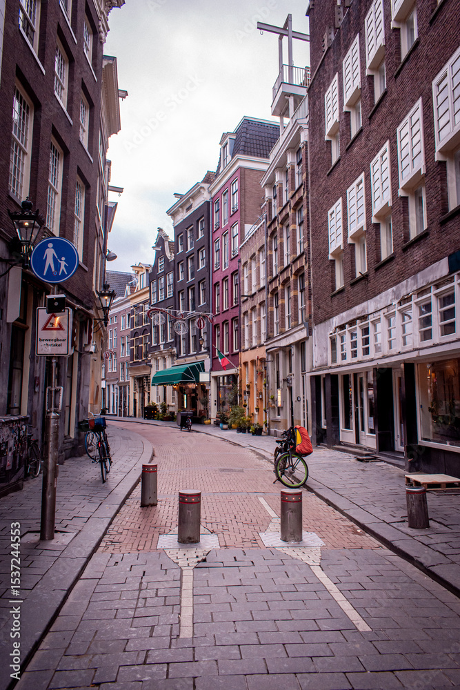 Obraz premium A narrow street in Amsterdam, lined with beautiful, colorful houses, various cafes and pubs, with bicycles parked along the way.
