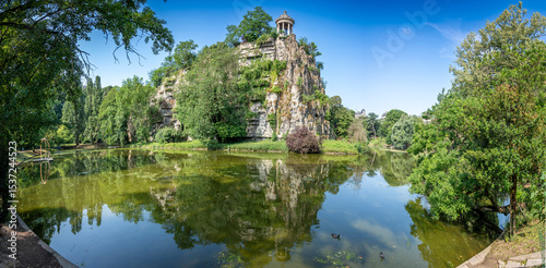 Paris, France - 06 14 2025: Buttes-Chaumont Park. View the central part of the park with belvedere island, Temple of the Sibyl, the lake, remarkable trees and vegetation