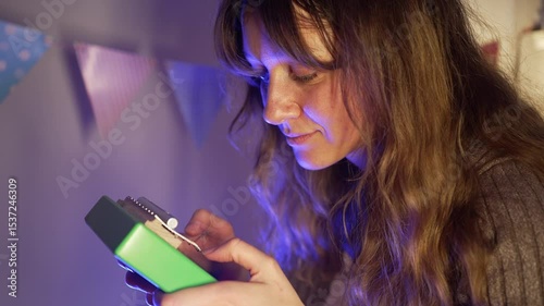 Young female musician playing green kalimba, creating melodic sounds while illuminated by soft blue light in decorated room with vibrant atmosphere