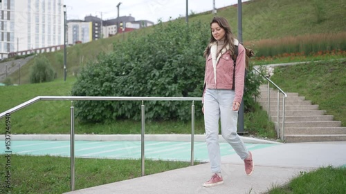Young woman strolling through urban park, walking confidently while waiting for romantic first date, embodying casual student lifestyle and youthful anticipation