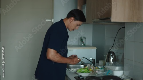 Young Asian male coiner carefully chopping fresh vegetables while preparing a nutritious meal