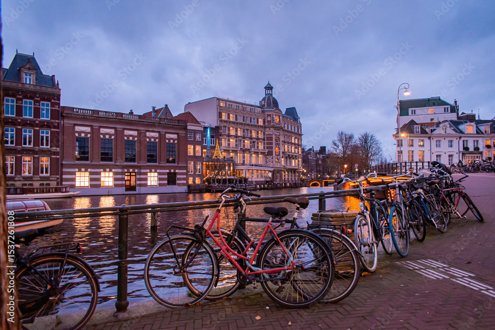 Fototapeta premium Nighttime Amsterdam. Along the canal, beautiful buildings with cafes and restaurants create a lively atmosphere. Bicycles are parked along the streets.