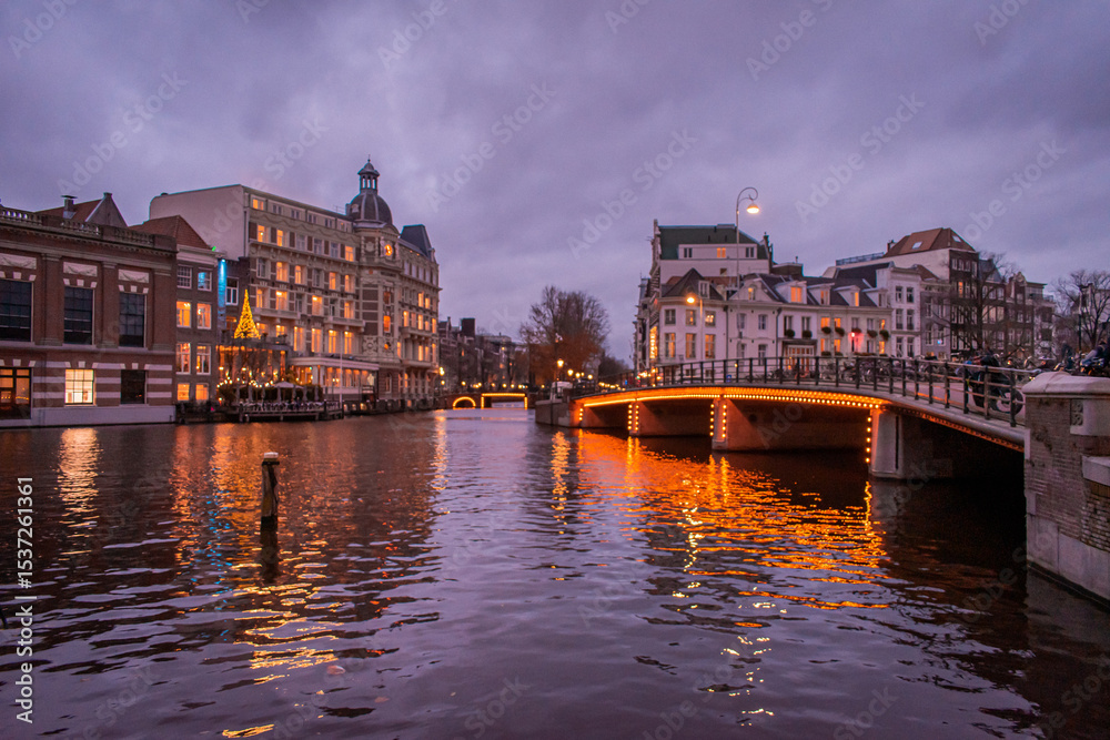 Obraz premium A picturesque canal scene in a city Amsterdam, showcasing a row of tall, narrow buildings with traditional European facades. Several houseboats are moored along the water.