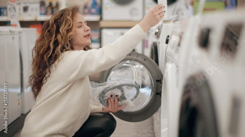 Customer carefully examining washing machines in electronics store, comparing features and specifications while browsing product display in slow motion, exploring potential home appliance purchase