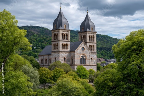 Basilica of St Matthias a stone church with twin towers framed by green trees stands against a cloudy sky and forested hills