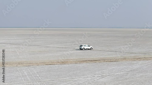 Aerial drone shot showing a white car driving under the vast sky over the Rann of Kutch salt desert. photo