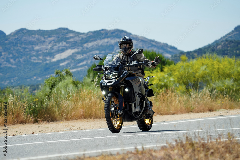 Fototapeta premium Motorcyclist waving while riding adventure motorcycle on scenic mountain road