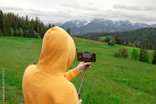 Young guy in a yellow hoodie films a mountain landscape with a camera