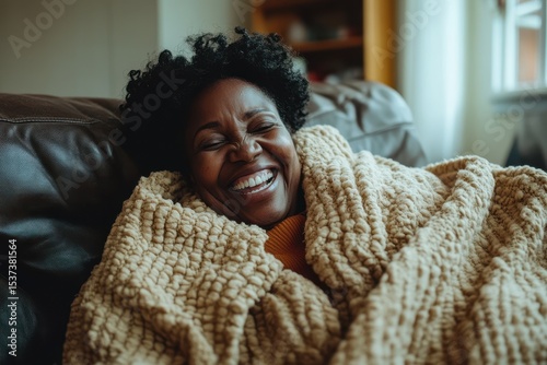 Cheerful Middle Aged Hispanic Woman Relaxing at Home with a Blanket, Laughing Comfortably in a Sweater