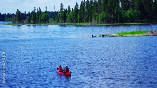 Canoes and people paddling on a calm mountain lake during a bright summer morning. Peaceful outdoor activity surrounded by colorful nature in a serene landscape.

