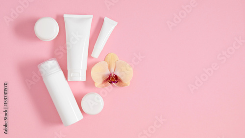 Set of cosmetic products white bottles and containers laid out on pastel pink background and beautiful orchid. Top view, flat lay.